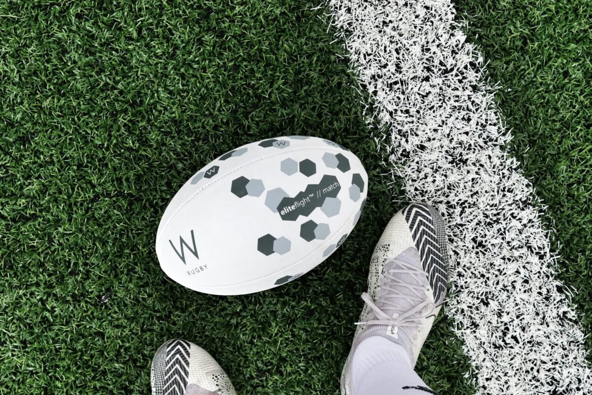 Detailed close-up of rugby boots and ball on a grass field line.