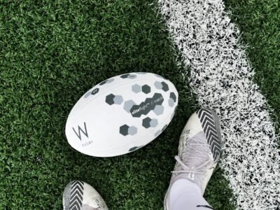 Detailed close-up of rugby boots and ball on a grass field line.